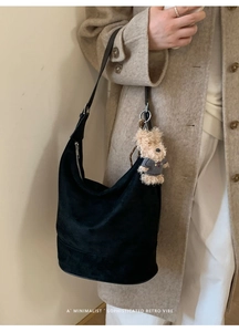 Chic black suede shoulder bag with cute brown teddy bear pendant on beige wool coat