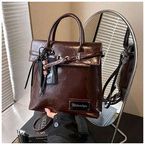 Détail d'un sac cabas en cuir marron foncé brillant avec plaque de marque et breloque