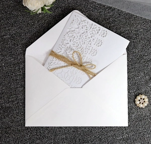 Detail of laser-cut wedding invitation with white lace pattern and rustic twine bow