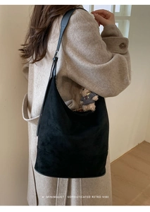 Black suede hobo tote bag with a cute plush bear pendant shown on a model in beige coat