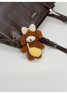 Close-up of cute brown curly plush puppy charm with plaid bow on a leather tote bag
