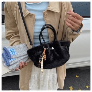 Detail einer schwarzen Plüsch-Handtasche aus Kunstpelz mit Holzperlenanhänger und Gurt
