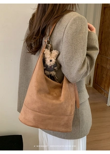 Brown suede hobo bag shown on shoulder with cute bear plush charm in a minimalist setting