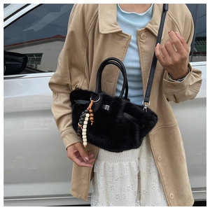 Detail einer schwarzen Kunstfell-Handtasche mit runden Griffen und Vintage-Perlen-Anhänger