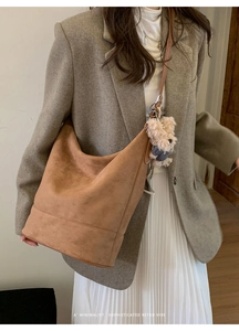 Brown suede bucket bag with plush bear charm worn by a model in a retro style outfit