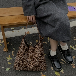 Grote shopper met luipaardprint en bruine leren handgreep op een houten bankje