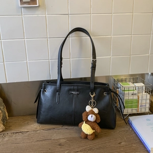 Dettaglio della borsa tote in ecopelle nera con targhetta in metallo e ciondolo a orsetto
