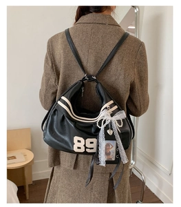 Dettaglio zaino nero in pelle sintetica con ricamo numero 89 vintage e ciondoli perle