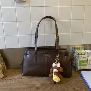 Dettaglio della borsa tote in pelle marrone scuro con cinghie regolabili e ciondolo orso