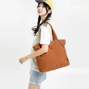 Detail of tan nylon tote bag showing side drawstring and brand logo label on surface