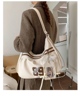 Dettaglio della borsa beige con toppa 89 e ciondolo con fiocco di pizzo e perle
