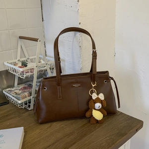 Detailed view of a brown faux leather tote bag with a plush bear charm on a wood table