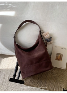 Brown suede hobo bag with a cute navy teddy bear pendant in a cozy indoor setting