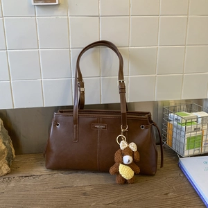 Dettaglio della borsa tote in pelle marrone opaca vintage con un ciondolo a forma di cane