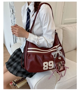 Borsa bordeaux con toppa 89 e fiocco in pizzo mostrata su un divano bianco elegante