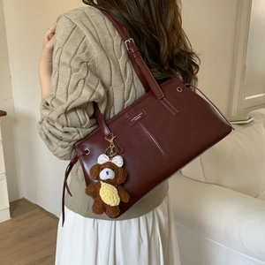 Dettaglio borsa tote in pelle bordeaux con logo argento e ciondolo orsetto di peluche