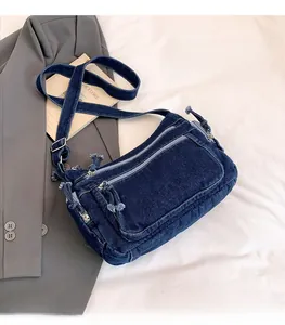 Close-up of deep blue denim crossbody bag with multiple zippers on white bedding