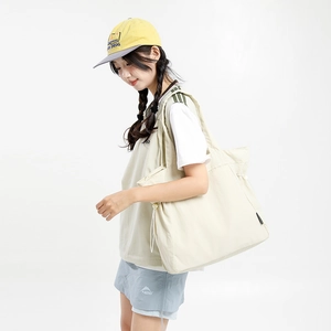 Detail view of beige nylon tote bag featuring side drawstrings and brand label detail