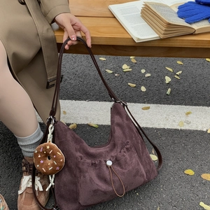 Detalle de bolso medialuna de ante vintage con colgante de donut de felpa en banco de madera