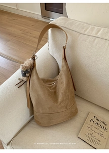 Close-up of brown suede hobo bag with plush charm on a beige sofa in a cozy home setting