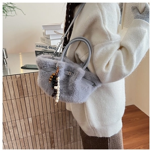 Details der grauen Kunstpelz-Handtasche mit dekorativen Holzperlen und weicher Textur