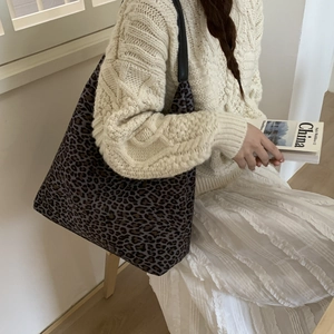 Detail van een grote tote bag met luipaardprint en zwarte leren riemen op een model