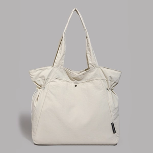 Detail of off-white tote bag showing textured fabric, drawstring side and metal snap button