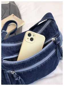 Detail showing denim crossbody bag capacity with smartphone and silver zippers