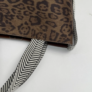 Close-up of leopard print suede bag with zig-zag pattern woven strap and cross stitching