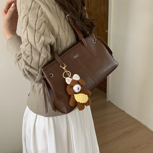 Dettaglio della borsa tote in pelle marrone scuro con targhetta e ciondolo a orsetto