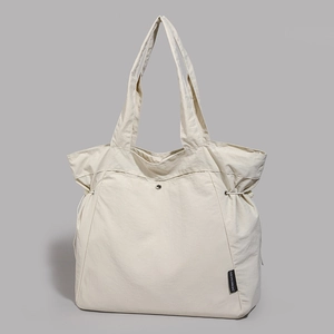 Detail of off-white nylon tote bag with drawstring side and branded black woven label