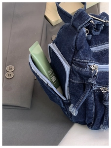 Close-up of dark blue denim crossbody bag featuring contrast stitching and multiple zippers