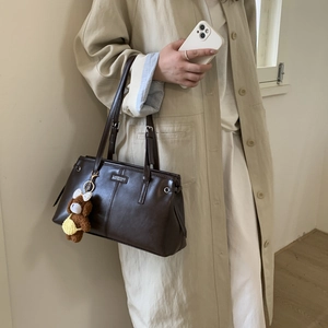 Dettaglio borsa tote in pelle marrone con ciondolo a orsetto indossata con trench beige