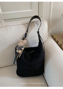 Detail of black suede tote bag with plush bear charm on a soft beige fabric sofa