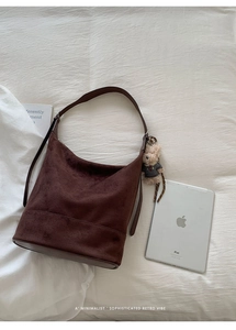 Detail of dark brown suede bucket bag featuring a soft texture and a cute plush bear charm
