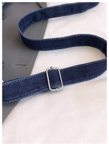Detailed macro view of denim shoulder strap with silver buckle and white stitching