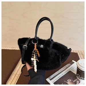 Detail einer schwarzen Plüschhandtasche mit Ledergriff und bunten Perlen als Anhänger