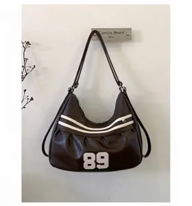 Dettaglio borsa hobo vintage in pelle PU marrone con strisce bianche e toppa numero 89