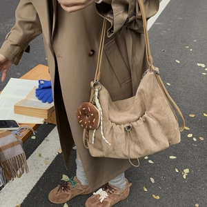 Detalle de bolso tote de ante caqui con bolsillo frontal con cordón y colgante de donut
