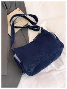 Detail of dark blue denim crossbody bag showing fabric texture and silver buckles