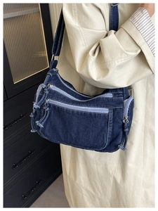 Detail of dark blue denim crossbody bag with multiple zipper pockets and fringe tassels