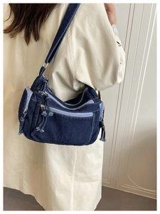 Detail of blue denim crossbody bag with multiple zip pockets on camel trench coat