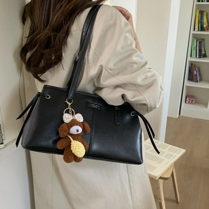 Dettaglio della borsa tote in ecopelle nera con ciondolo a forma di cane di peluche e logo