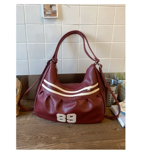 Dettaglio borsa tote vintage bordeaux con strisce bianche e numero 89 su tavolo legno