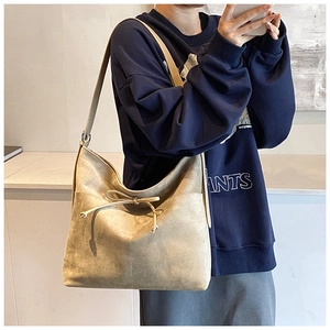 Detail view of a beige suede tote bag featuring a decorative drawstring bow and metal rings