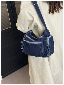 Detail view of deep blue denim crossbody bag with multi-zipper pockets and metal buckle