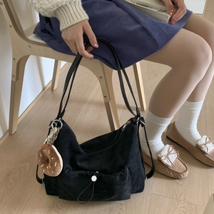 Detalle de bolso de hombro en ante negro con bolsillo frontal de cordón y colgante donut