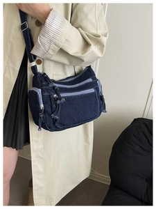 Detail of dark blue denim crossbody bag featuring multiple zipper pockets and strap