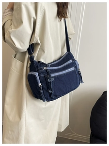 Detailed macro of dark blue denim crossbody bag featuring multiple contrast zippers