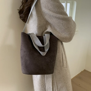 Detail of dark brown suede bucket bag with black and white herringbone strap on a model